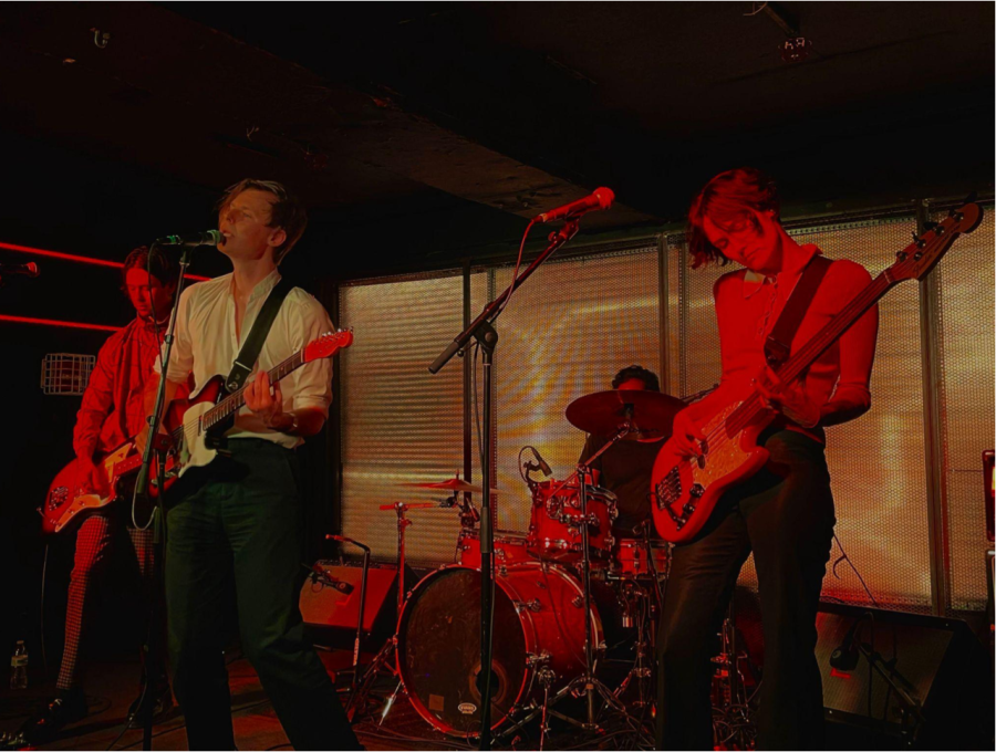Photo Six: Dear Boy performing on stage. All four members are pictured, from right to left: Austin Hayman, guitar and backing vocals, Ben Grey, guitar and lead vocals, Keith Cooper, drums, and Lucy Lawrence, bass and backing vocals.
